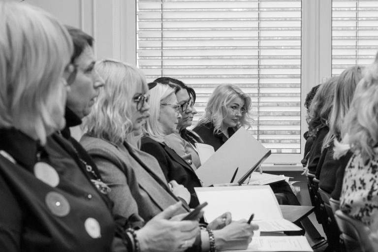 personeelsbeleid — Black and white image of women in a meeting, attentively taking notes.