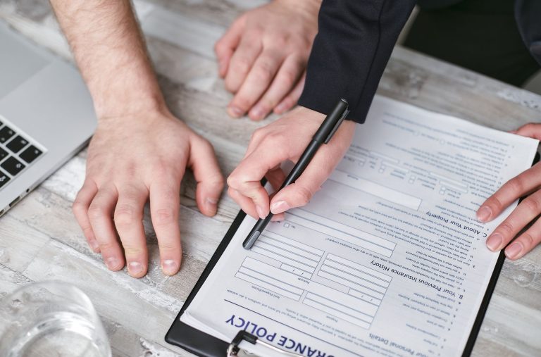 personeelsbeleid voorbeeld — Close-up image of two people signing an insurance policy document on a wooden desk.