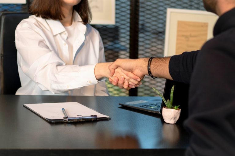salarisonderhandeling jonge werknemers — a man and a woman shaking hands in front of a laptop